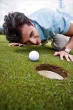 Hispanic man looking at golf ball near cup