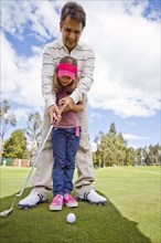 Hispanic man teaching girl to play golf