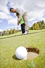 Hispanic man teaching boy to play golf