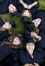 Hispanic graduates in caps and gowns laying in grass