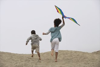 Mixed race children running on beach with kite