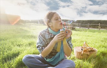 Mixed race woman blowing bubbles in sunny field