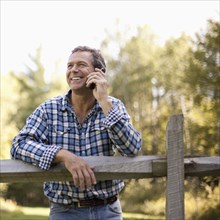 Caucasian man leaning on fence talking on cell phone