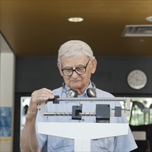 Senior man weighing himself in health club