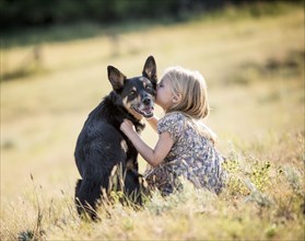 Caucasian girl sitting in field kissing dog