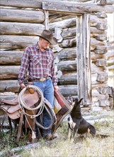 Caucasian man holding saddle and blanket looking at dog