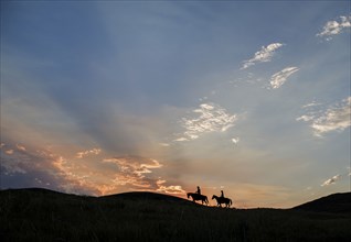 Silhouette of Caucasian couple riding horses at sunset