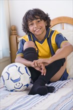 Mixed Race boy with soccer ball on bed