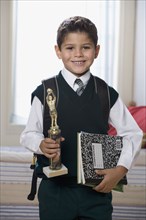 Hispanic boy holding trophy and school books