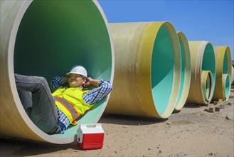 Caucasian construction worker napping inside large pipe