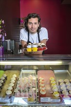 Hispanic business owner showing cupcakes bakery display case