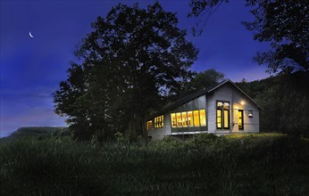 Illuminated cabin with clapboard siding on landscape at night