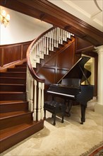 Baby grand piano at foot of large winding staircase