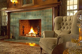 Comfy armchair next to green tile fireplace with fire