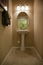 Oval mirror with wall lamps at pedestal washbasin at home