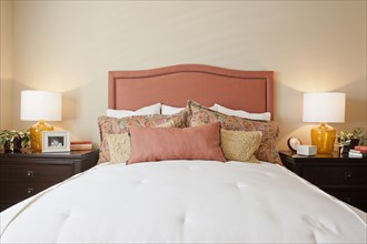 Arranged pillows on tidy bed with lit table lamps in the bedroom at home