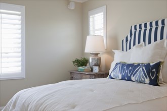 Arranged pillows on tidy bed with lit table lamp in the bedroom at home