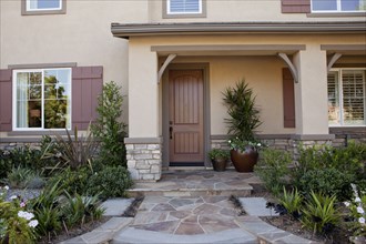 Walkway along plants leading to a house with closed brown door