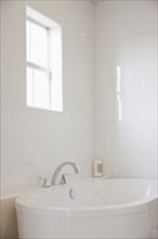 Close-up of a white bath with tiled wall and window in the bathroom
