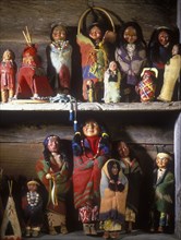 Vintage Native American dolls on display on shelves in rustic log home. Very colorful.