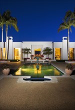 Evening exterior of a large white modern house with a swimming pool