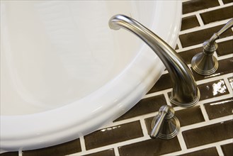 Detail of chrome faucet and brown tile.