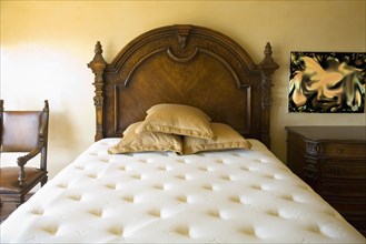 Large unmade bed with three pillows and wooden headboard