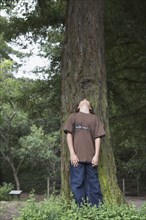 Mixed race boy leaning on tree trunk