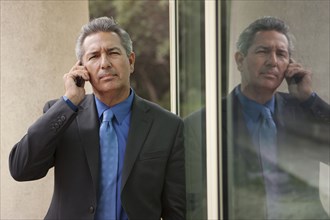 Hispanic businessman leaning on window talking on cell phone