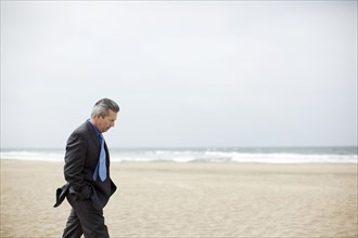 Pensive Hispanic businessman walking on beach