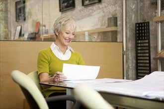 Smiling Caucasian businesswoman reading paperwork in office