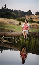 Reflection in lake of Caucasian woman sitting on log