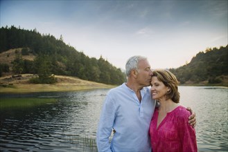 Man kissing woman on forehead near lake