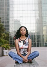 Portrait of serious mixed race woman sitting near highrise