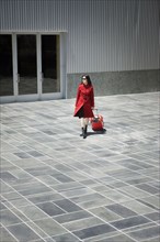 Asian woman pulling rolling suitcase near building