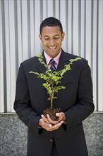 Smiling mixed race businessman holding seedling