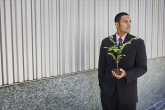 Pensive mixed race businessman holding seedling