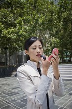 Asian woman applying lipstick outdoors