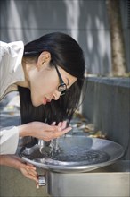 Asian woman leaning over water fountain