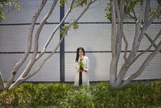 Asian woman holding flower near trees