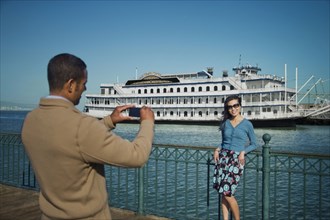 Man photographing woman at waterfront