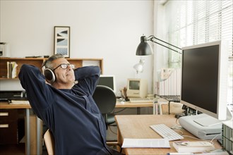 Hispanic businessman relaxing at desk and listening to headphones