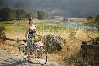 Smiling Hispanic woman standing with bicycle near river