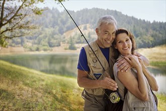 Couple with fishing rod hugging near river
