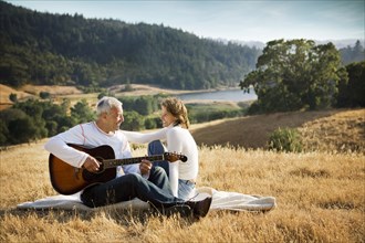 Man sitting on blanket in field playing guitar for woman