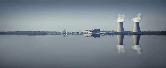 Smoke stacks and factory reflected in still lake