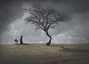 Man in black robes with baby carriage by dead tree