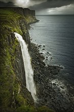 Waterfall over rocky cliff and sea