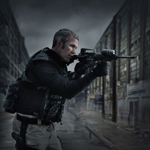 Caucasian sniper aiming gun on city street