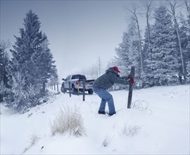 Man repairing wooden post in snowy ground